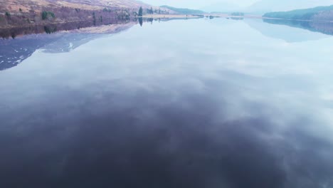 Stunning-epic-aerial-drone-view-of-calm-glass-like-water-reflection-lake-of-Loch-Lochy-in-Scotland,-tilt-down