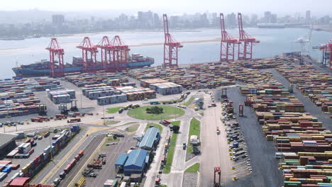 Drone-aerial-shot-towards-a-large-container-cargo-ship-being-loaded-by-gantry-cranes-with-the-shipping-container-yard-in-foreground