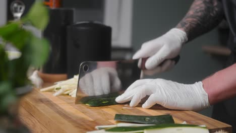 Fresh-zucchini-being-chopped-on-a-wooden-board-by-young-professional-male-chef-in-an-elegant-black-shirt-with-tattoos