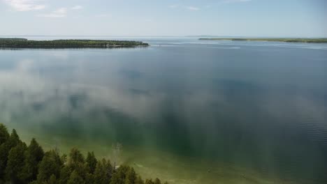 Aerial-Backwards-of-Calm-Lake-Water-Over-Forested-Island,-Hessel,-Michigan