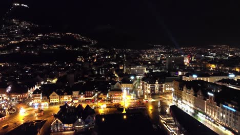 Upward-moving-aerial-from-above-sea-close-to-Bergen-fishmarket---Revealing-full-city-view-and-Floyen-hillside-in-background---New-years-eve-with-random-fireworks-exloding,-Norway