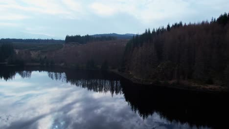 Aerial-drone-flying-above-peaceful-calm-lake-of-Loch-Lochy,-water-reflection,-rising-reveal-forest-landscape