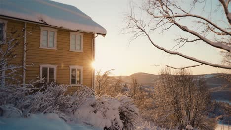 Golden-sunrise-behind-yellow-house-during-snowy-winter-day-in-Norway,Europe