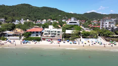 Aerial-drone-scene-of-luxury-lodging-houses-and-apartments-facing-the-sea-with-many-people-having-fun-on-the-beach-in-Jurere-Internacional-Florianópolis