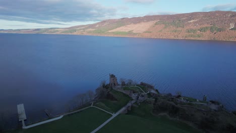 Aerial-drone-shot-of-Urquhart-Castle-ruins-sitting-by-Loch-Ness-lake,-Scotland
