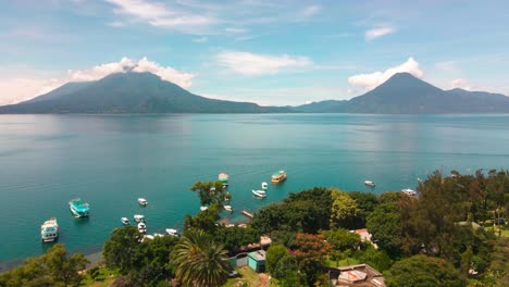 Aerial-Flyover-of-Village,-Beach-and-Boats-toward-Lake-and-Volcanoes---Lake-Atitlan,-Panajachel,-Guatemala---Summer