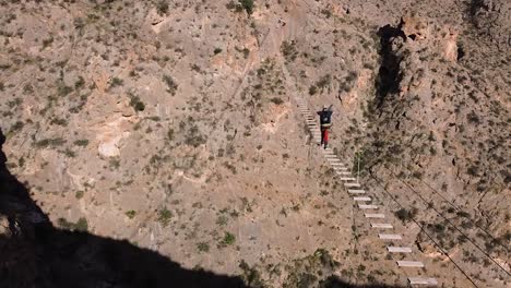 Sportman-crossing-suspended-bridge-between-mountains-in-via-ferrata