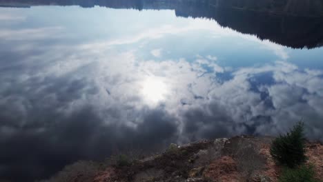 Aerial-tilting-mirroring-clouds-and-sun-of-sky-in-pure-water-of-tranquil-Loch-Lochy-lake-in-Spean-Bridge,-Scotland,-water-reflection-of-cloudscape-drone