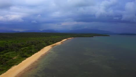 From-above,-the-drone-captures-a-stunning-view-of-the-tropical-beach-as-it-emerges-from-the-clouds,-its-beauty-and-tranquility-undimmed-by-the-grey-skies-overhead