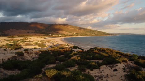 Low-drone-shot-swooping-over-Tarifa's-coastline-at-sunset