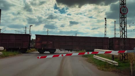 a-train-passes-through-a-railway-crossing-with-lowered-barriers-dramatic-sky