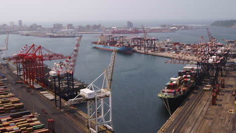 Wide-aerial-shot-of-Cargo-ships-being-loaded-with-shipping-containers-by-gantry-cranes-in-Durban-harbour-South-Africa