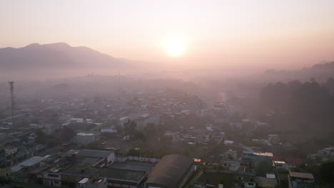 Aerial-footage-flying-through-the-early-morning-fog-of-a-beautiful-sunrise-in-San-Juan-Ostuncaclo,-Guatemala-with-the-buildings-of-the-city-in-the-foreground
