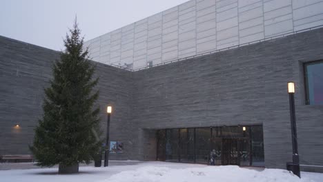 Snow-Falling-Out-The-National-Museum-of-Art,-Architecture,-and-Design-Entrance-With-Tree-In-Oslo,-Norway