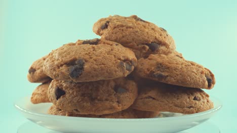 A-close-up-shot-of-a-white-plate-full-of-chocolate-chip-cookies,-on-a-360-rotating-stand,-studio-lighting,-slow-motion,-4K-video