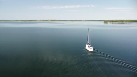 Aerial-of-Lone-Sailboat-Heading-Out-With-Calm-Water,-Hessel,-Michigan