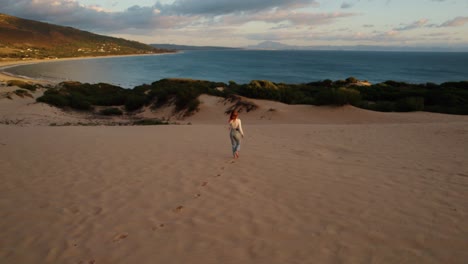 Drone-shot-of-a-young-woman-walking-on-Spain's-coast-at-sunset
