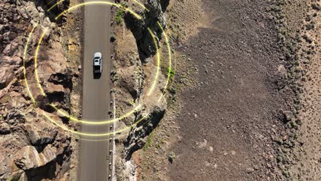 Top-down-aerial-shot-of-a-self-driving-car-making-its-way-through-a-steep-desert-cliff-roadway