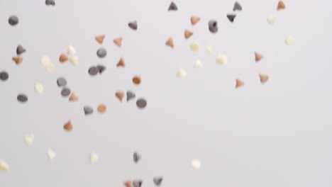 Medley-of-white-chocolate,-butterscotch-caramel-and-semi-sweet-chocolate-chips-raining-down-in-slow-motion-on-white-backdrop