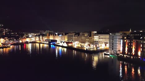 Nachtluftbild,-Das-Den-Fischmarkt-Von-Bergen-Und-Die-Innenstadt-Rund-Um-Strandkaien-Zeigt---Beleuchtete-Stadt-Mit-Reflexionen-Im-Ruhigen-Fjord