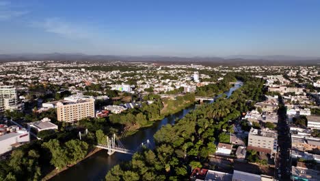 Aerial-overview-of-Río-Tamazula-river-and-the-cityscape-of-Culiacan-city,-golden-hour-in-Sinaloa,-Mexico