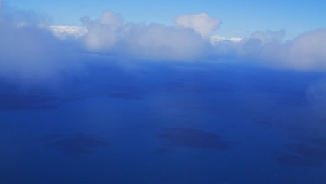 A-view-from-a-plane-captures-the-breathtaking-sight-of-going-through-the-clouds-above-the-sea,-showcasing-the-beauty-of-the-white-fluffy-clouds-contrasting-with-the-deep-blue-of-the-ocean