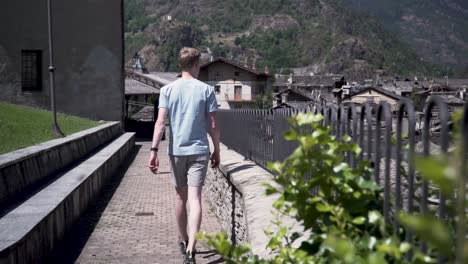Man-in-shorts-and-a-t-shirt-walking-beside-an-old-fence-overlooking-a-typical-picturesque-old-Italian-village