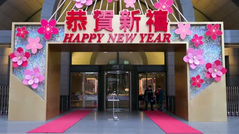 La-Gente-Entra-A-Un-Edificio-Que-Muestra-Un-Mensaje-De-Celebración,-Feliz-Año-Nuevo,-Para-El-Año-Nuevo-Lunar-Chino-En-Hong-Kong