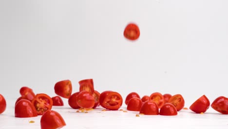 Fresh,-bright-red-halved-cherry-tomato-fruits-and-vegetables-landing-down-and-bouncing-on-white-table-top-in-slow-motion