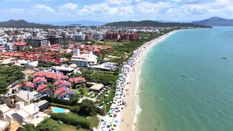 Aerial-scene-of-tourist-beach-in-florianopolis-with-many-hotels-houses-and-buildings-facing-the-sea-with-many-accommodations-summer-season-and-sand-with-many-people-sunbathing-in-jurere-international