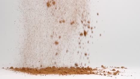 Chocolate-brown-cocoa-powder-ingredient-for-baking-falling-into-pile-on-white-table-in-slow-motion