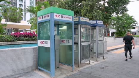 Chinese-pedestrians-walk-past-public-telephone-booths,-also-called-payphones,-as-they-are-rapidly-dying-out-and-disappearing-in-the-age-of-smartphones-and-the-internet