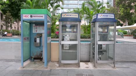 Pedestrians-walk-past-public-telephone-booths,-also-called-payphones,-as-they-are-rapidly-dying-out-and-disappearing-in-the-age-of-smartphones-and-the-internet