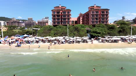 Drohnen-Luftaufnahme-Des-Touristischen-Strandes-In-Florianopolis,-Brasilien,-Mit-Vielen-Hotels-Mit-Blick-Auf-Das-Meer,-Vielen-Unterkünften-Für-Die-Hochsommersaison-Und-Sand-Mit-Vielen-Menschen,-Die-Sich-In-Jure-International-Sonnen