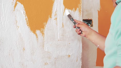 Cute-Boy-Wearing-Cap-Using-Painting-Brush-To-Paint-Orange-Wall-Into-White-Color
