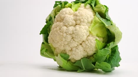 Whole-head-of-fresh-cauliflower-encased-in-green-leaves-landing-and-bouncing-on-white-table-top-in-slow-motion