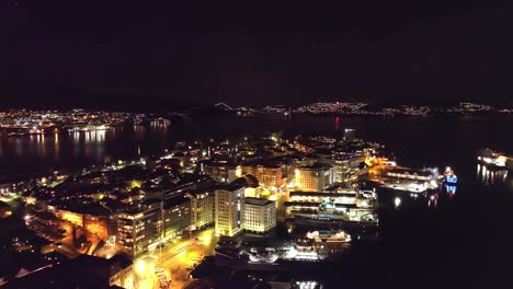 Nordnes-area-and-byfjorden-Bergen-during-early-new-years-eve---Beautiful-night-aerial-with-illuminated-city-and-random-fireworks-seen-in-Askoy-island-background