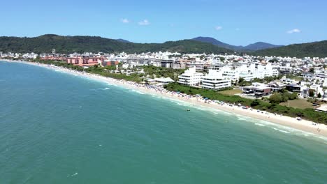 Aerial-drone-scene-of-upscale-touristic-beach-in-Florianopolis-Brazil-with-many-people-on-the-beach-and-buildings-in-front-of-the-sea-with-beautiful-blue-ocean-jurere-internacional