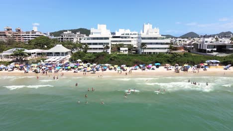 Luftdrohnenszene-Des-Gehobenen-Touristischen-Strandes-In-Florianopolis-Brasilien-Mit-Vielen-Menschen-Und-Konstruktionen-Am-Strand-Und-Gebäuden-Vor-Dem-Meer-Mit-Wunderschönem-Blauem-Ozean-Jurere-Internacional