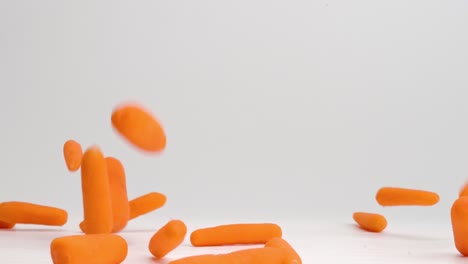 Bright-orange-baby-carrots-raining-down-onto-white-table-top-and-bouncing-in-all-directions-in-slow-motion