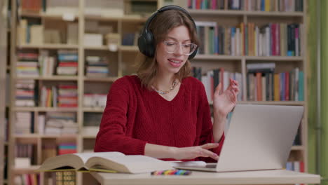 Young-woman-listening-to-audio-using-headphones-in-library