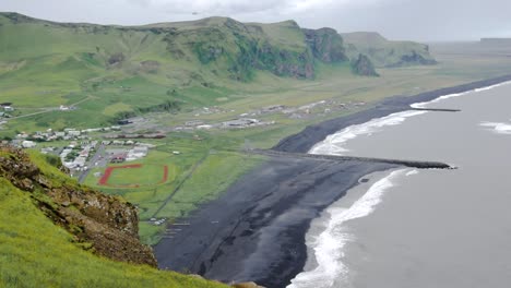 Static-landscape-view-of-the-small-town-of-Vík-í-Mýrdal,-Iceland-during-a-cloudy-day,-with-grassfields-and-black-sand-beach