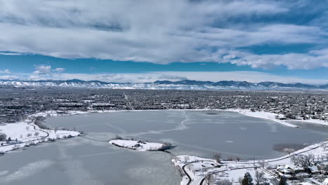 Aerial-drone-shot-circling-moving-over-a-frozen-Sloan-Lake,-Denver-during-winter-storm-showing-Rocky-Mountains-in-background
