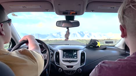 Driving-in-California-through-a-barren-landscape-towards-snow-covered-mountain-range