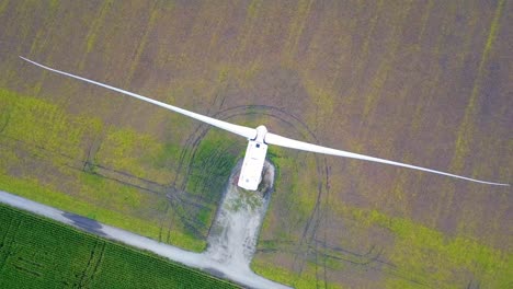 Orbiting-aerial-view-looking-down-at-wind-turbines-spinning-blades-on-green-cultivated-farmland-field