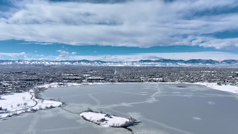 Aerial-drone-moving-backwards-to-reveal-frozen-Sloan-Lake,-Denver-during-winter-storm-showing-Rocky-Mountains-in-background