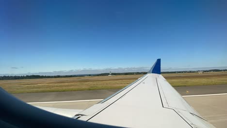 Window-view-of-passenger-airline-taking-off-from-JFK-airport-amidst-clear-blue-skies