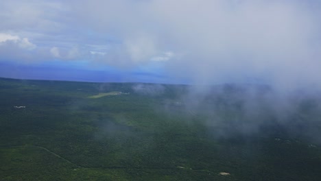A-view-from-a-plane-captures-the-breathtaking-sight-of-flying-through-the-clouds-above-a-tropical-forest-island,-showcasing-the-beauty-of-the-fluffy-clouds-contrasting-with-the-green-vegetation