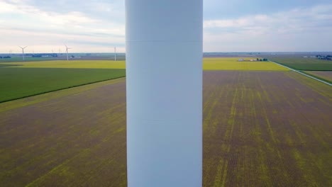 Aerial-view-rising-up-wind-turbine-mast-and-spinning-blades-overlooking-green-Indiana-farmland