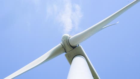 Low-angle-looking-up-at-spinning-wind-turbine-energy-generator-blades-against-blue-sky